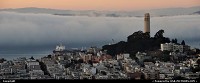 Coit Tower as the bay is flooded by the seasonal fog. A cargo ship is sailing into.